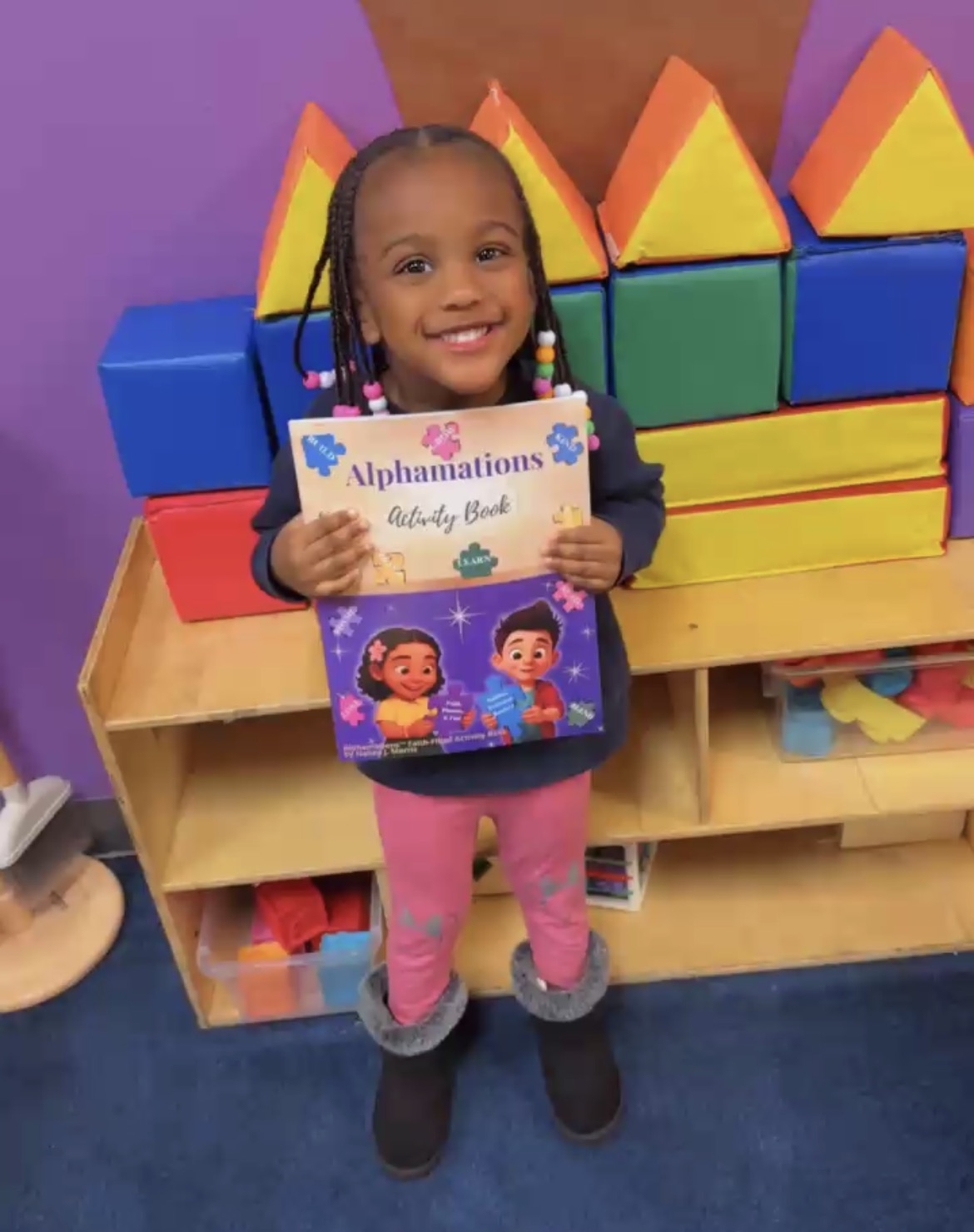 Young learner proudly holding the Alphamations™ Faith-Filled Activity Book, representing confidence, joyful learning, and early literacy development.